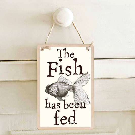 The fish has been fed / The fish has not been fed - Double-sided wooden mini sign.

Made from certified sustainable wood and printed on both sides with a fun, practical message and retro illustration.

15 × 10 cm sustainable wood, natural twine.&nbsp;

Light and durable, eco-friendly, ready to hang.

Made in Suffolk.