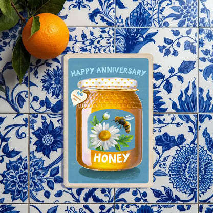 Anniversary card : Honey jar with a bee and daisy on a blue background, labeled 'Happy Anniversary Honey'. The wooden postcard company